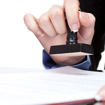 A person is holding a rubber stamp over papers.
