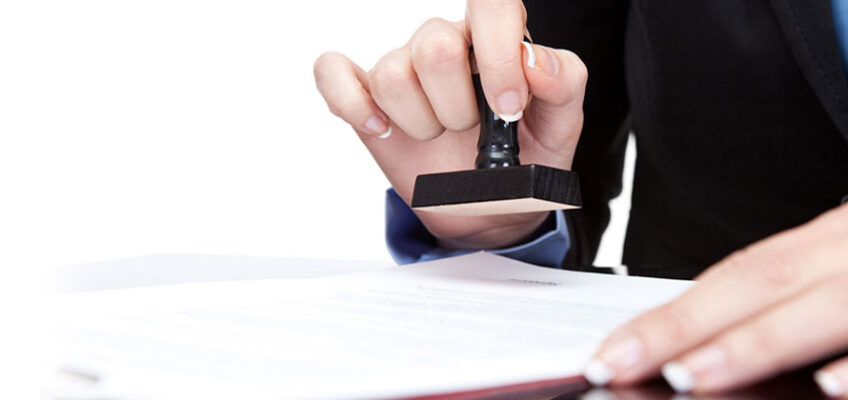 A person is holding a rubber stamp over papers.